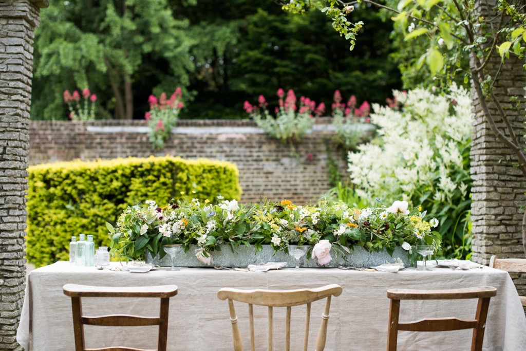 Garden with table in foreground, set with flower arrangement in a long metal trough